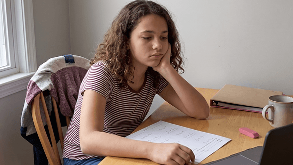 The same girl on day one, slumped over the math worksheet with her chin on her hand, stuck.